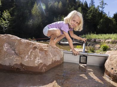 Das Element Wasser kann auf der Gartenschaut hautnah erlebt werden. Ein kleines Mädchen spielt mit einer Stauvorrichtung im Bach.